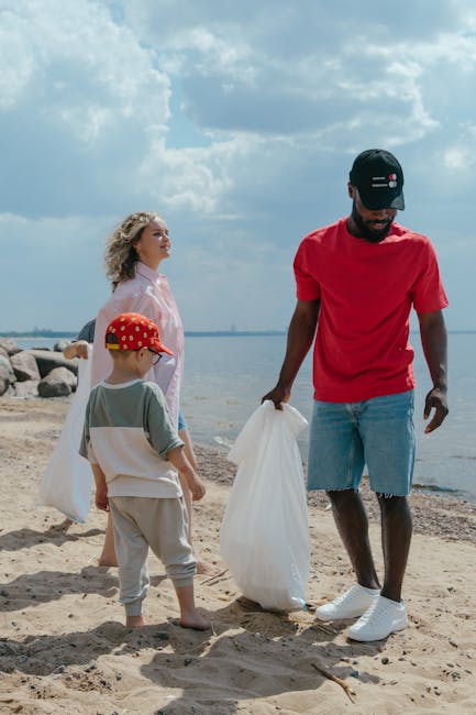 A group of three people, including an adult man and two children, are participating in a beach clean-up activity. The man, positioned on the right, is wearing a red T-shirt, light blue denim shorts wi